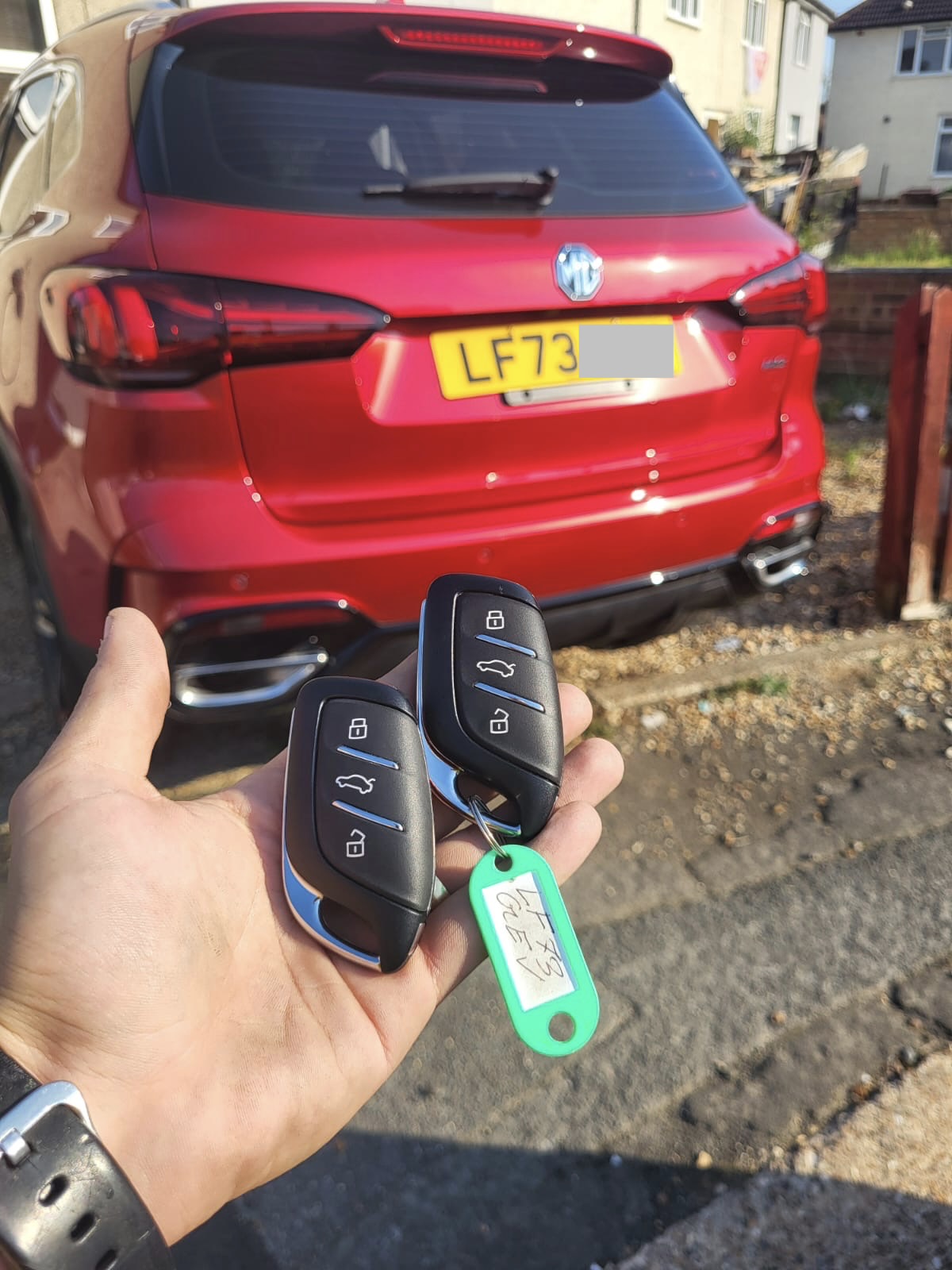 Two newly cut and programmed MG remote keys held in front of a red MG HS on a driveway