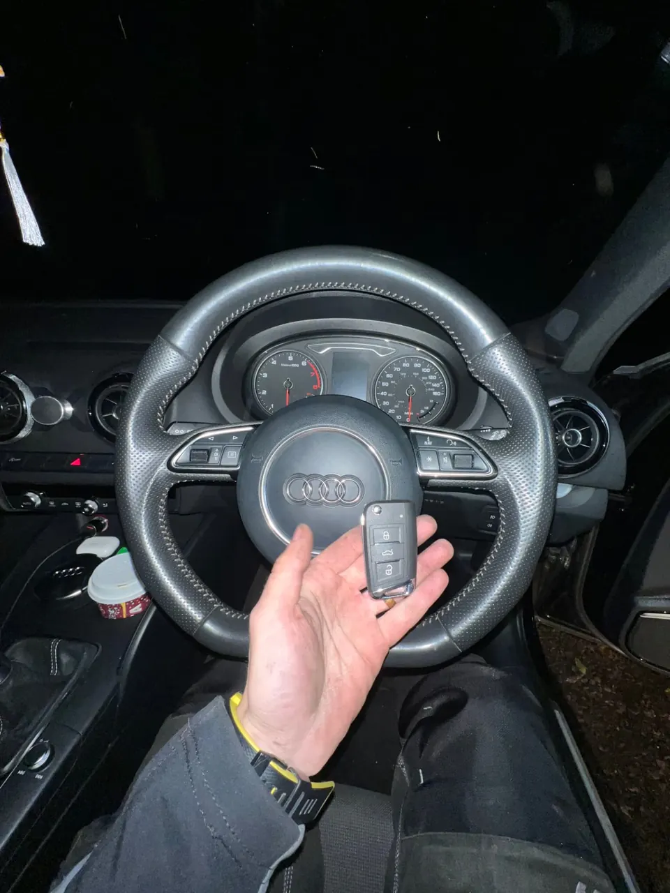 Audi flip key held in front of an Audi A3 steering wheel and instrument cluster