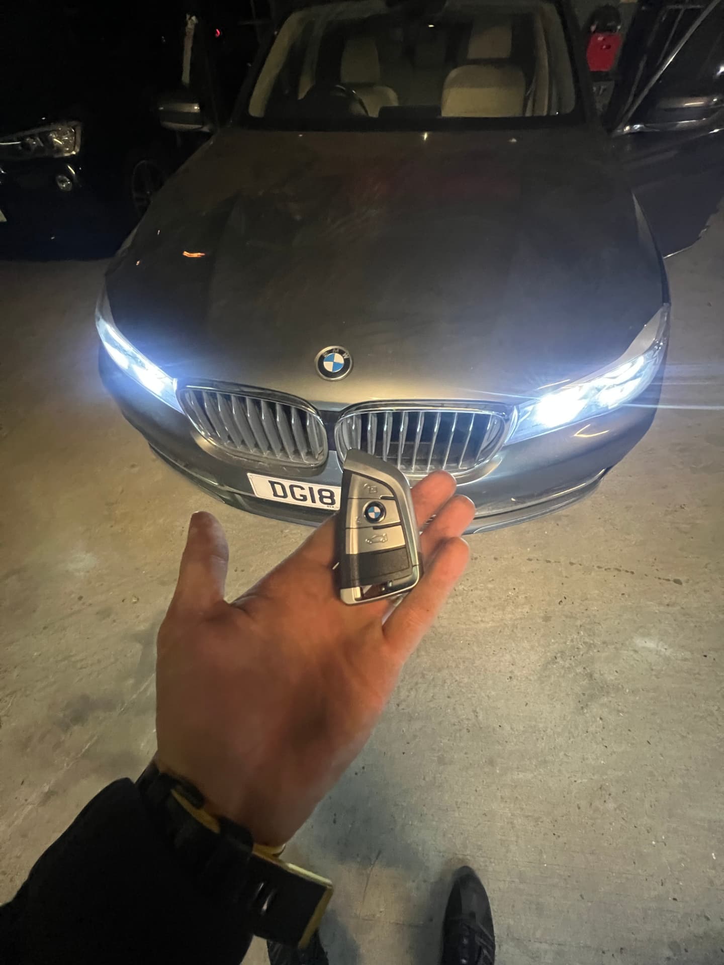 BMW smart key held in front of a grey BMW 5 Series with headlights on