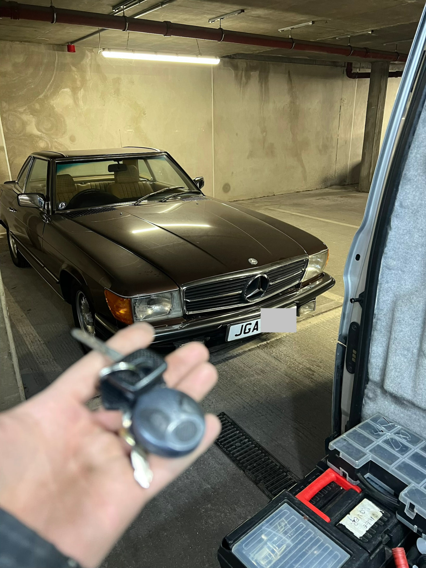 Mercedes-Benz keys held in front of a classic brown Mercedes SL in a garage
