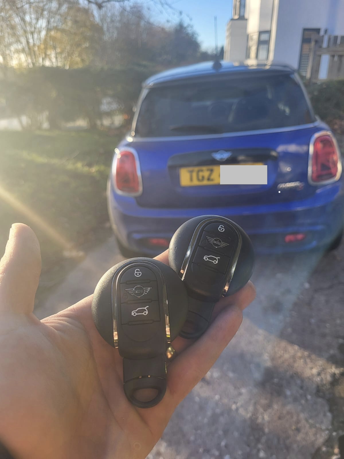 Two MINI proximity smart keys held in front of a blue MINI Countryman on a driveway