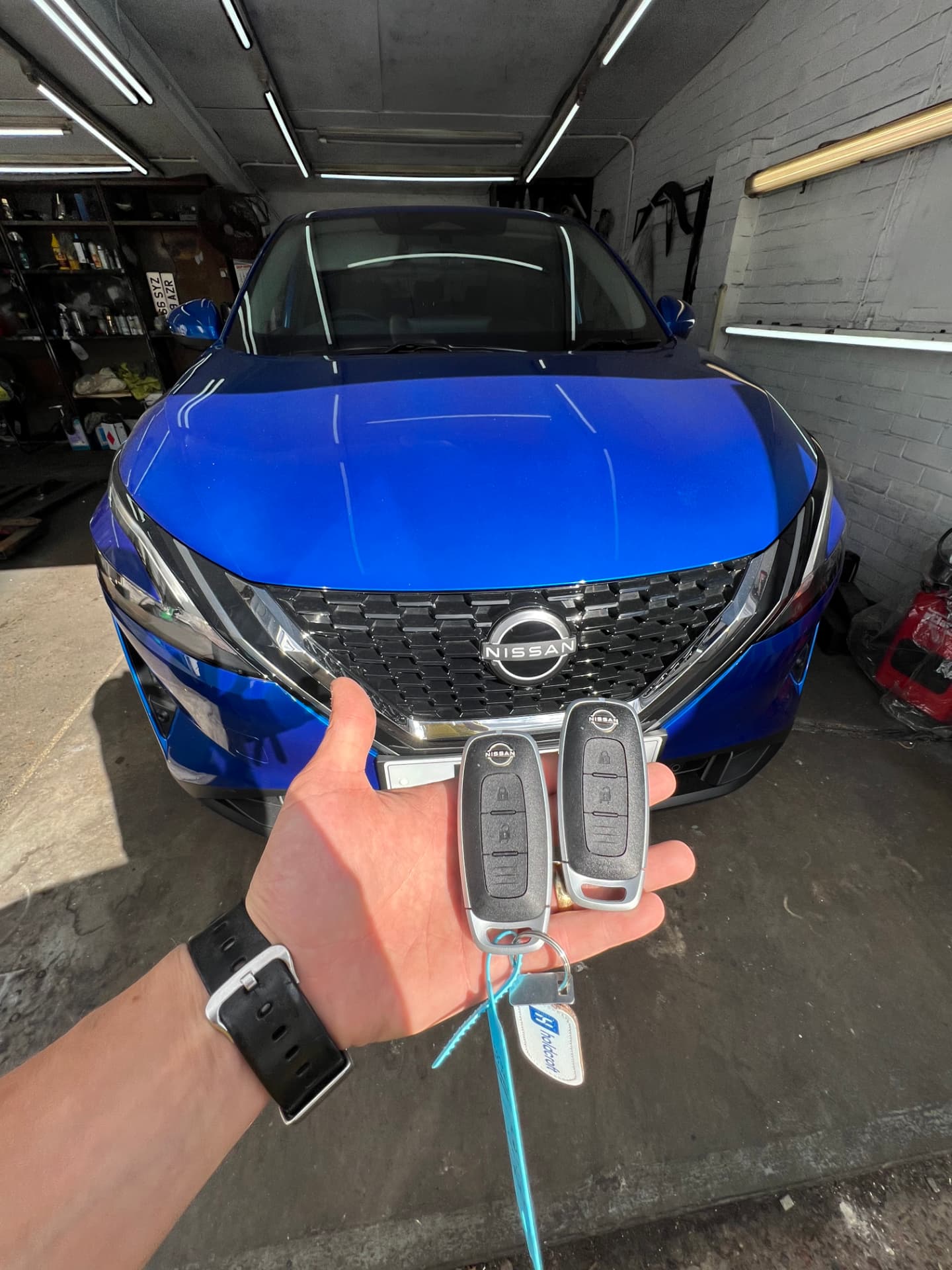 Two Nissan smart keys held in front of a blue Nissan