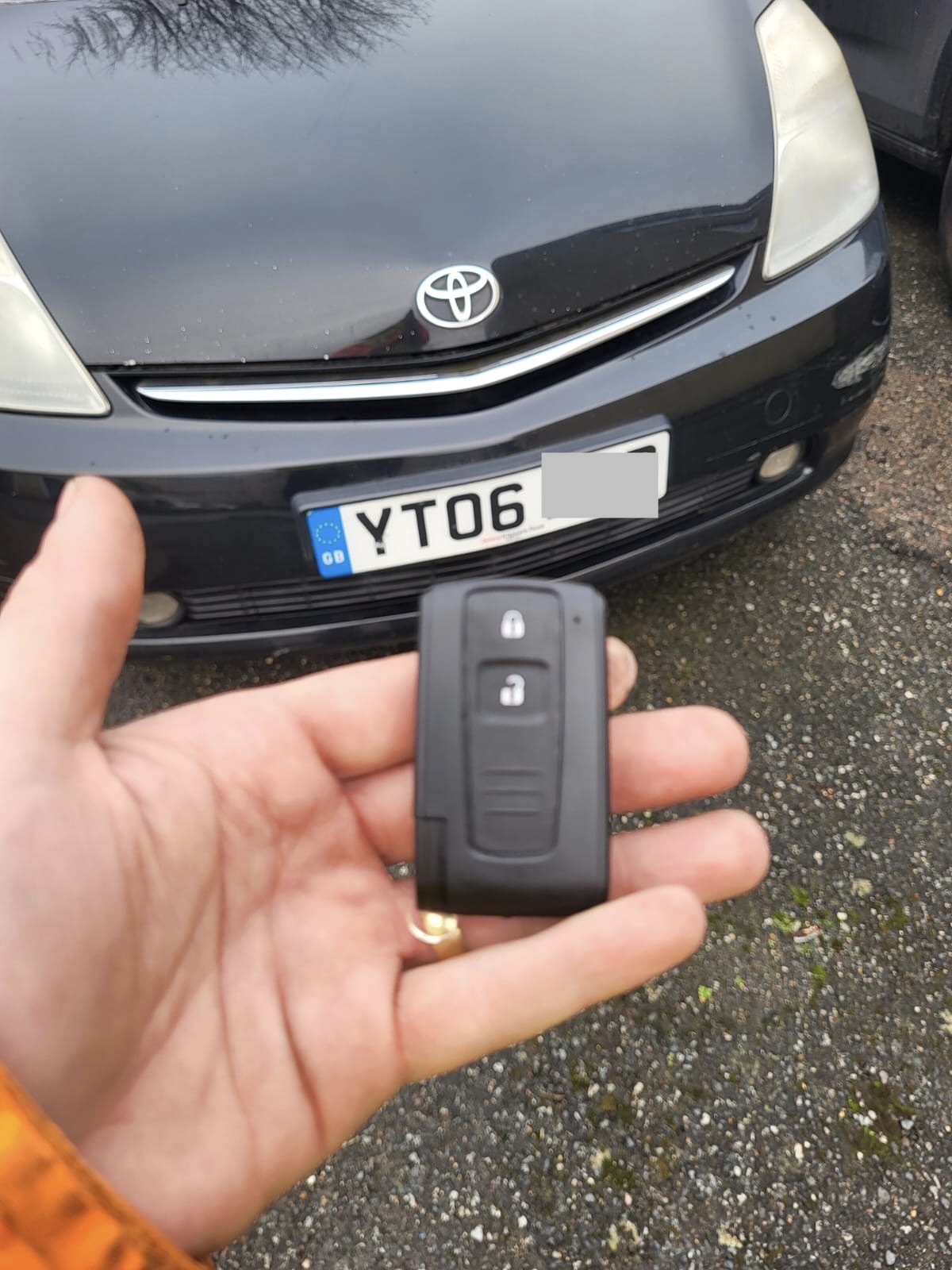 Toyota smart key card-style remote held in front of a black Toyota Prius