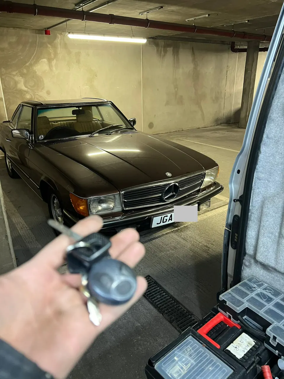Mercedes-Benz keys held in front of a classic brown Mercedes SL in a garage