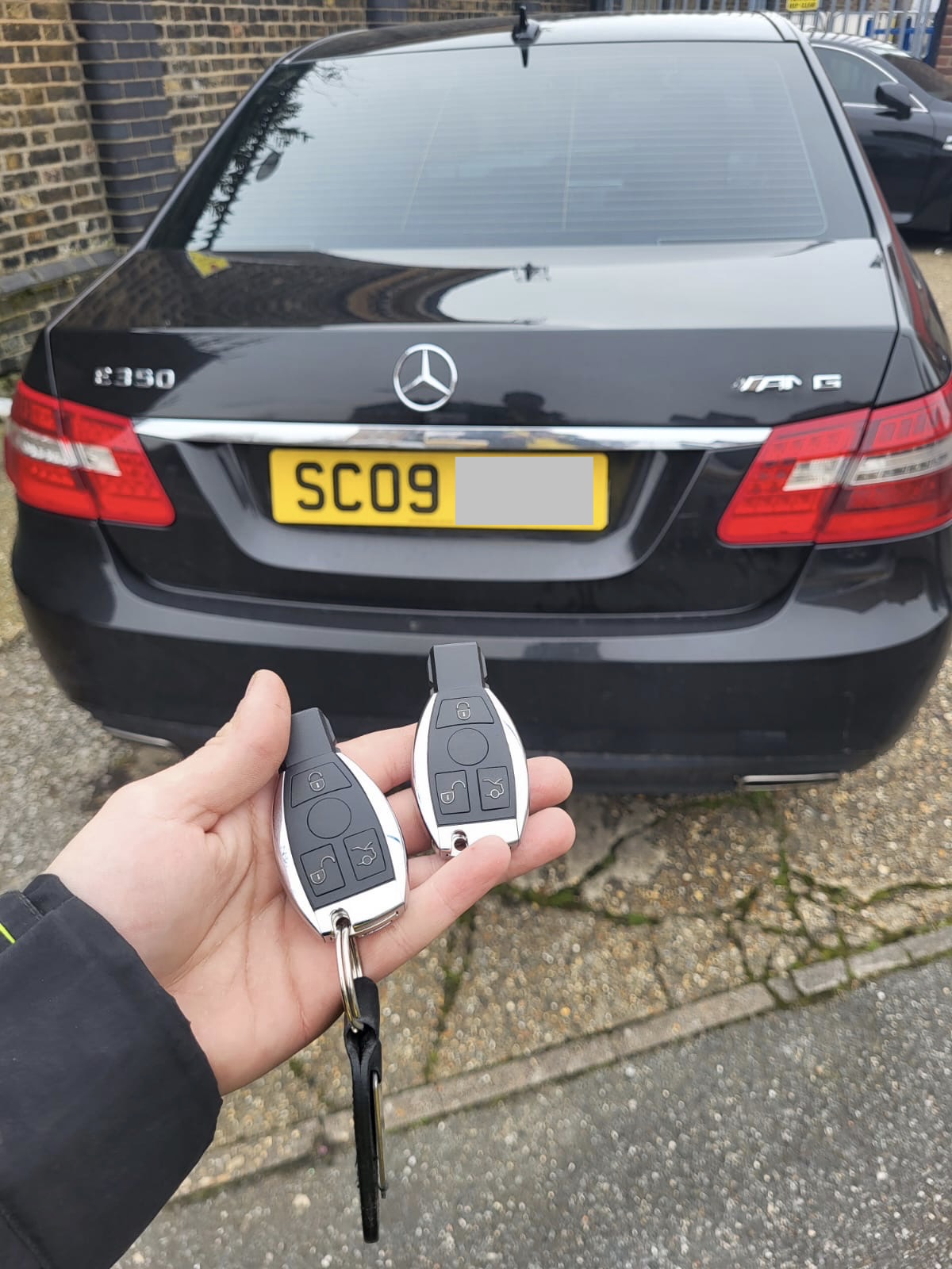 Two Mercedes chrome fob keys held in front of a black Mercedes E350 AMG