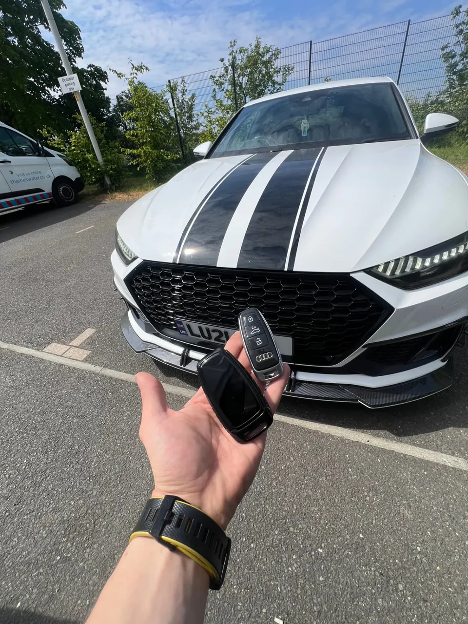 Two Audi smart keys held in front of a white Audi RS7 with black racing stripes