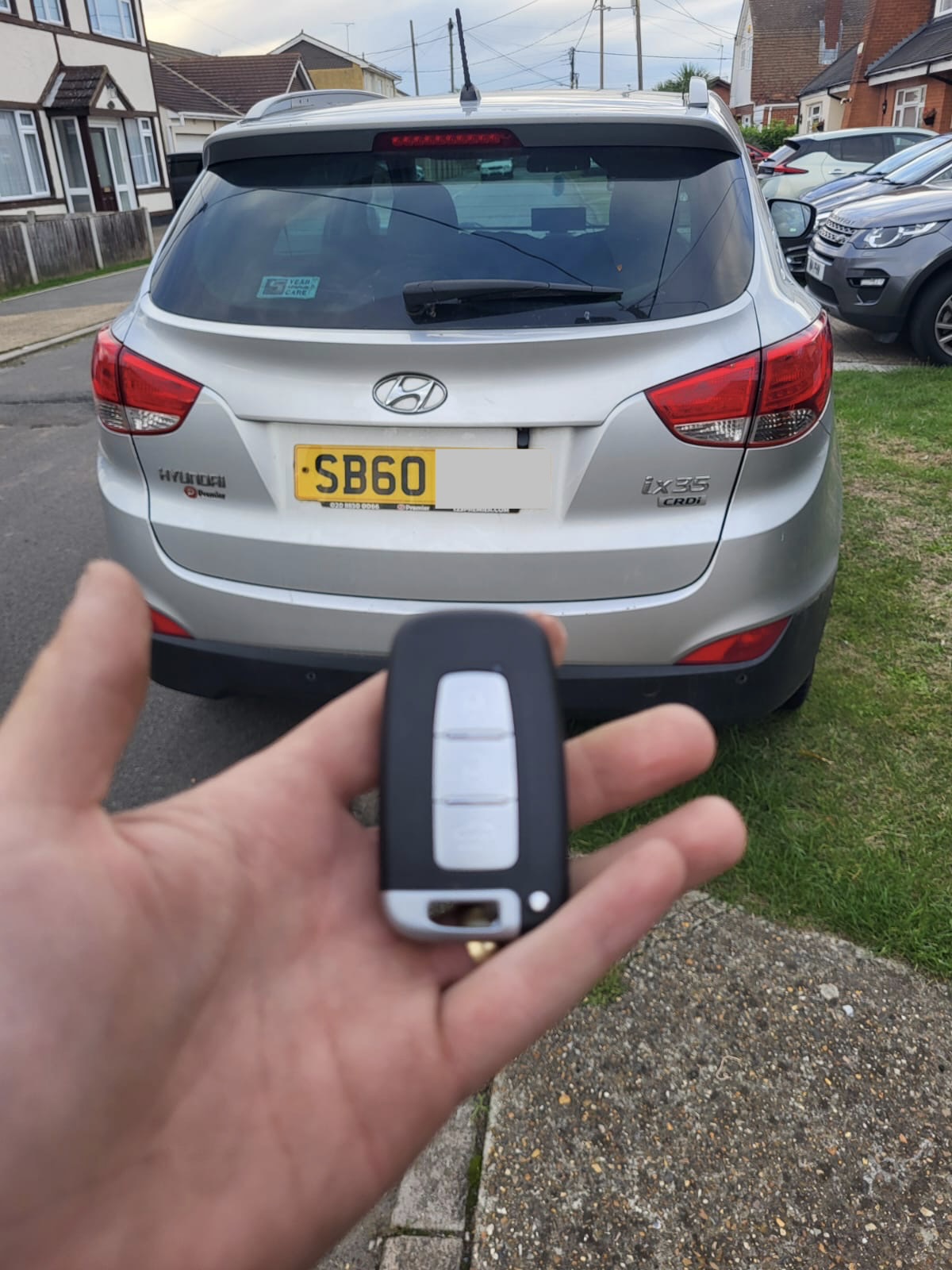 Hyundai smart key held in front of a silver Hyundai ix35 parked on a residential street