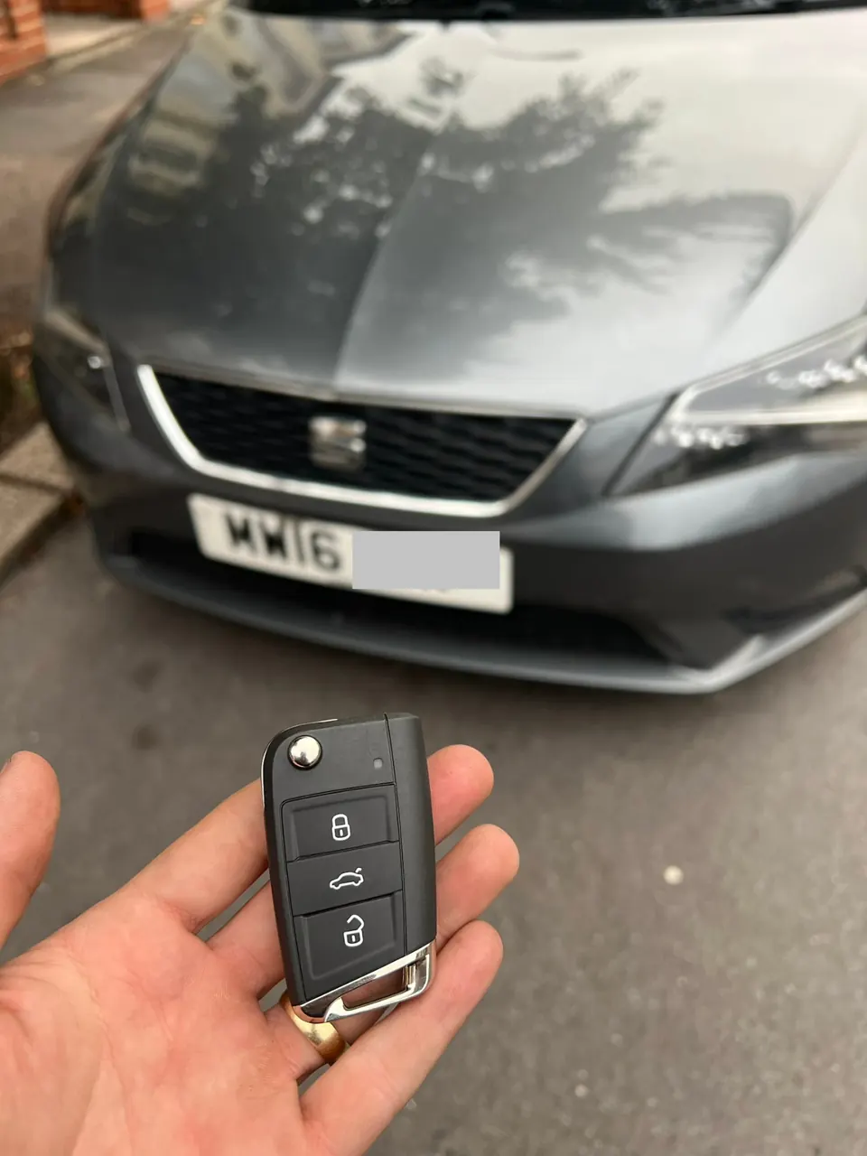 Seat flip remote key held in front of a grey Seat