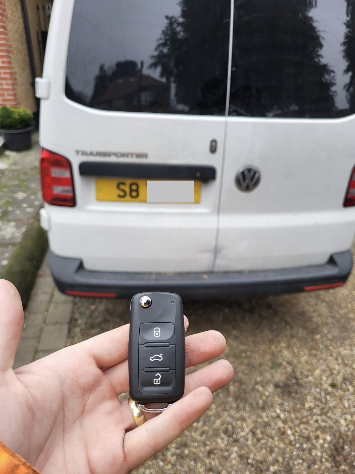 Volkswagen three-button flip key held in front of a white Volkswagen Transporter van