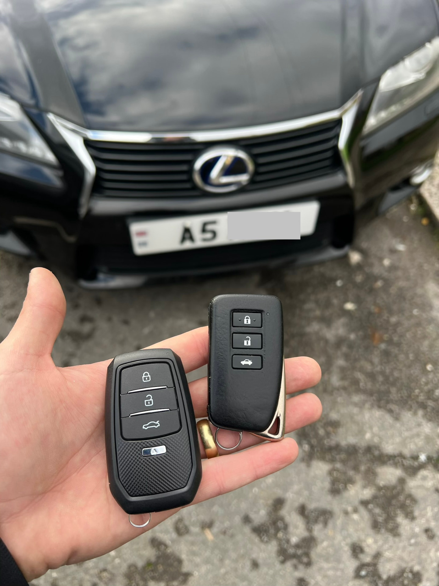 Two Lexus smart keys held in front of a black Lexus